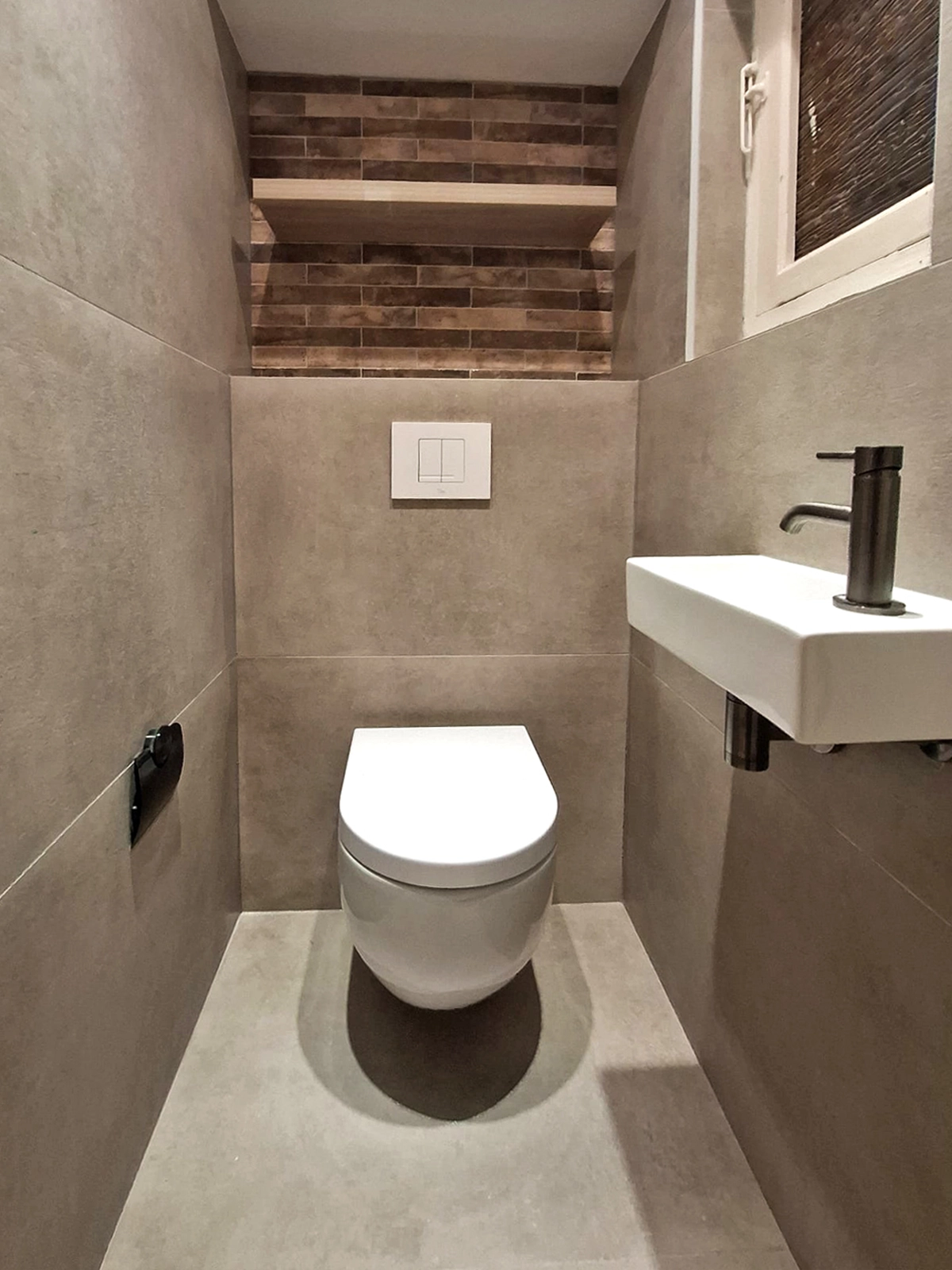 Moderne badkamer met houten badkamermeubel, ronde verlichte spiegel, wandtoilet, zwarte verwarming en wasmachinekast.