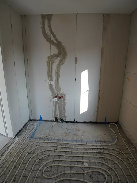 Badkamer in aanbouw met vloerverwarming, leidingwerk, wandplaten en voorbereid aansluitpunt voor wastafel.
