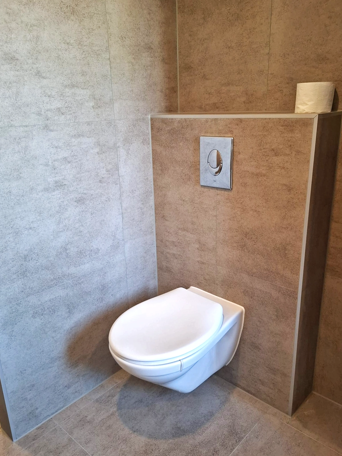 Moderne badkamer met dubbele waskommen, houten badkamermeubel, ovale verlichte spiegel, vrijstaand bad en grijze wandtegels.