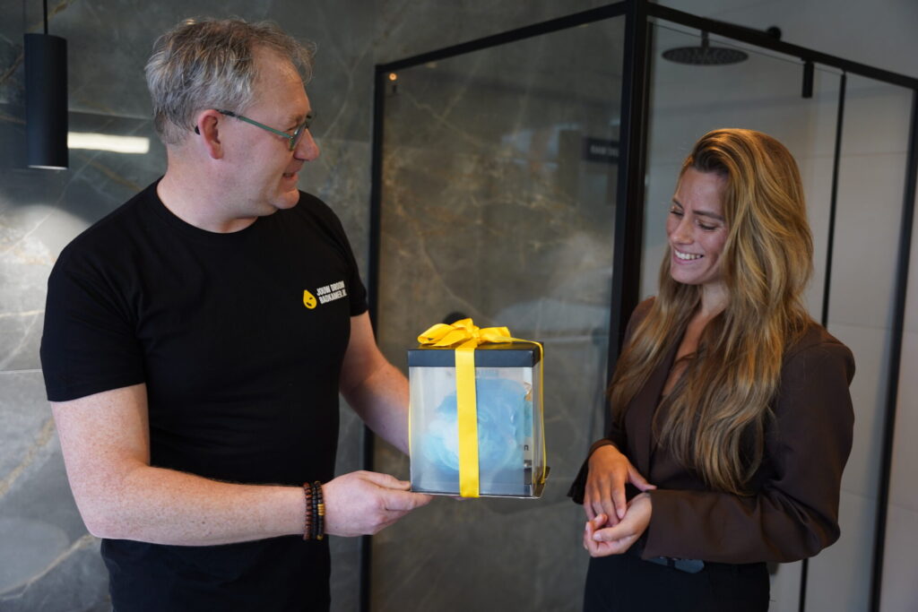 Badkameradviseur overhandigt cadeau aan klant in moderne badkamer showroom.