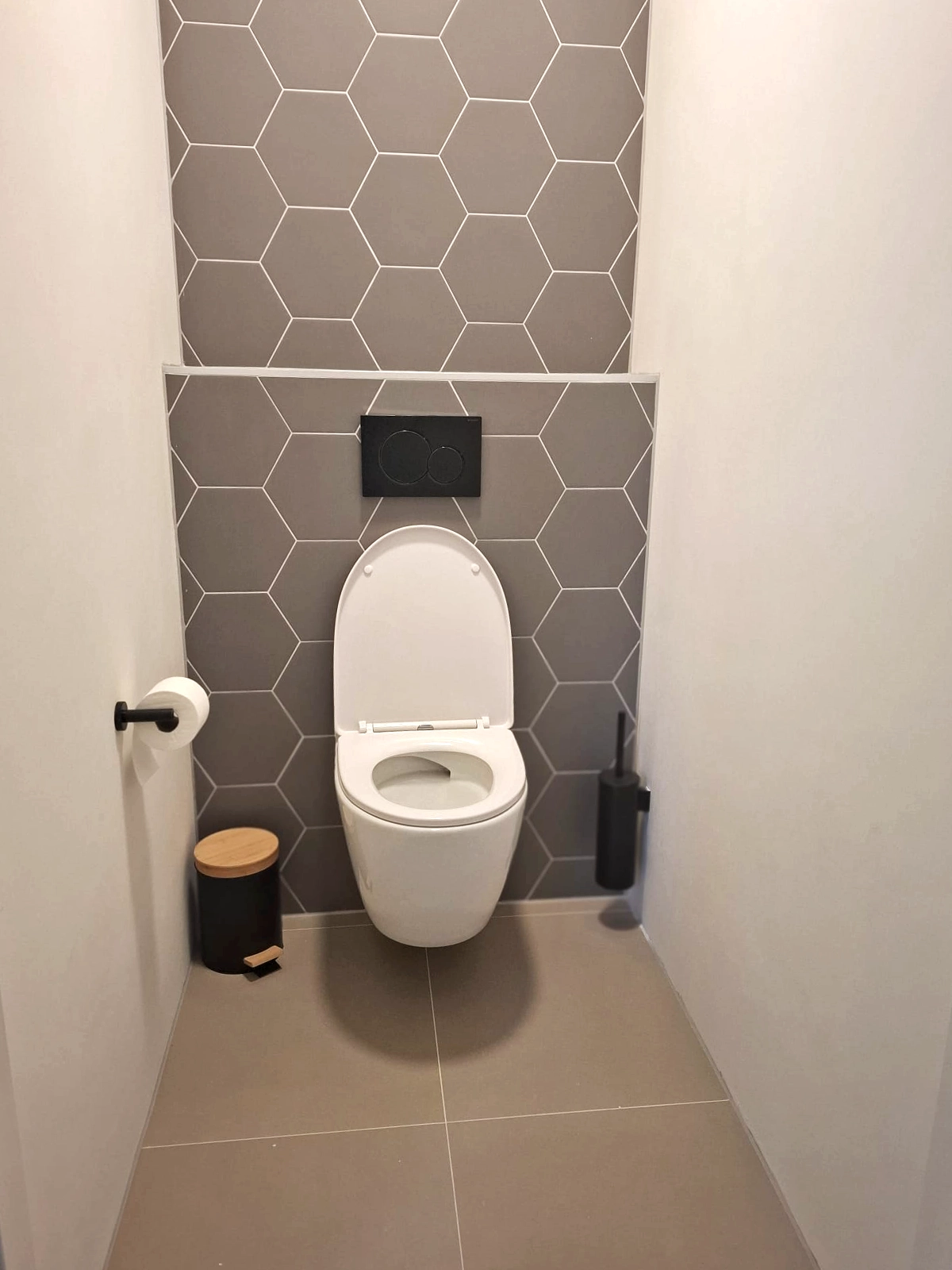 Moderne badkamer met donker badkamermeubel, zwarte kraan, spiegelkast, zwarte verwarming en beige tegels.