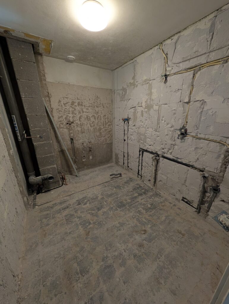 Ruwe badkamer in renovatiefase met zichtbare leidingen, elektra en voorbereidingen voor nieuw sanitair.