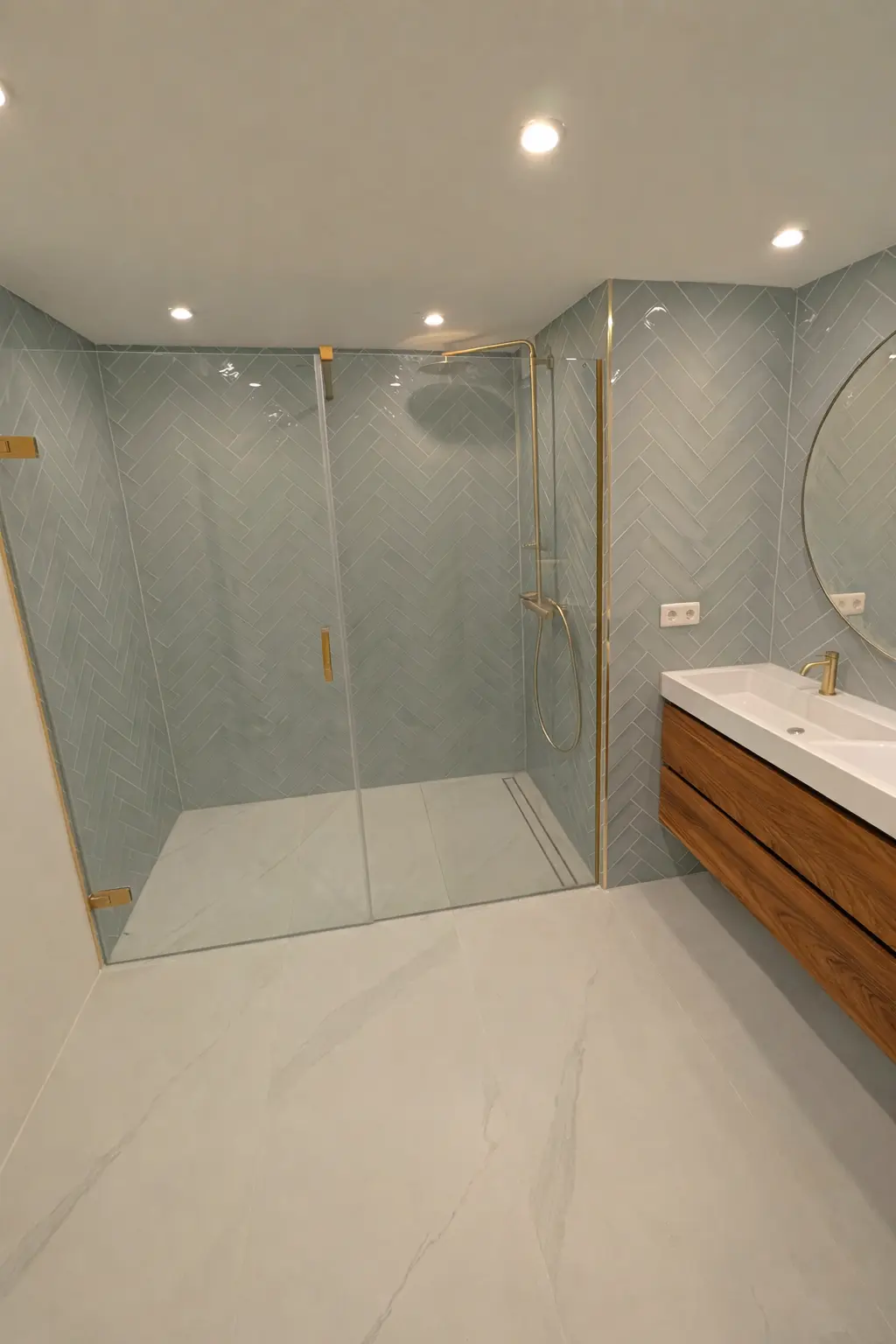 Moderne badkamer met ruime inloopdouche, lichtblauwe wandtegels in visgraatpatroon, glazen douchewand en houten badkamermeubel met dubbele wastafel.