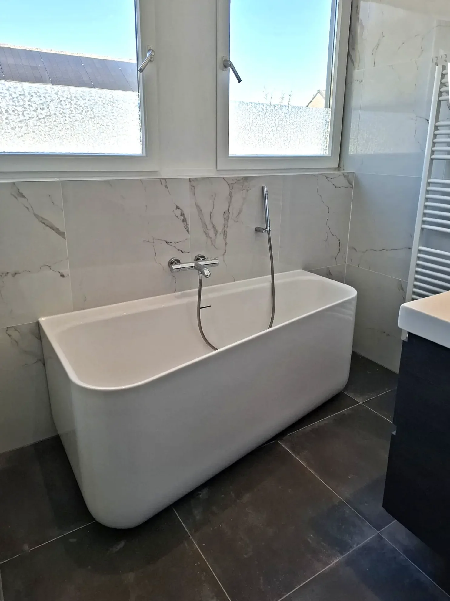Moderne badkamer met vrijstaand bad, marmerlook wandtegels en donkere vloertegels.