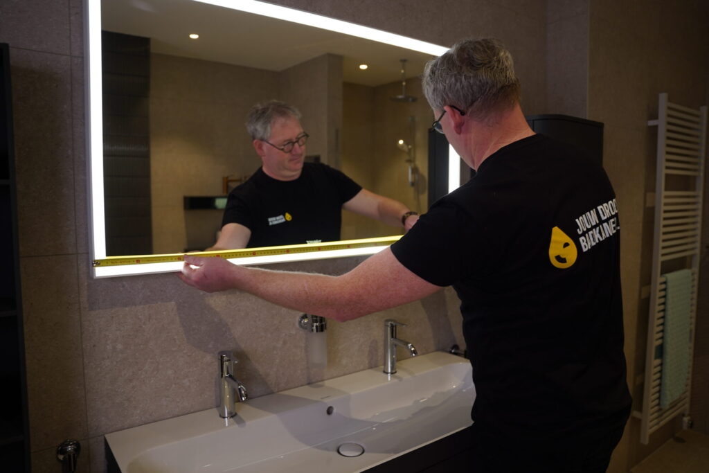 Medewerker van Jouw Droombadkamer meet een verlichte badkamerspiegel boven een modern badkamermeubel.