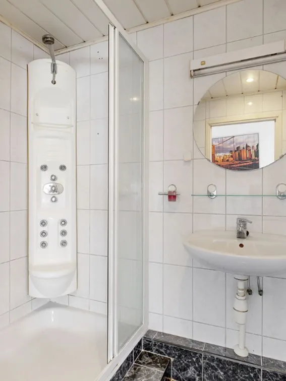 Badkamer met douchecabine, douchepaneel, ronde spiegel, wastafel en witte wandtegels.