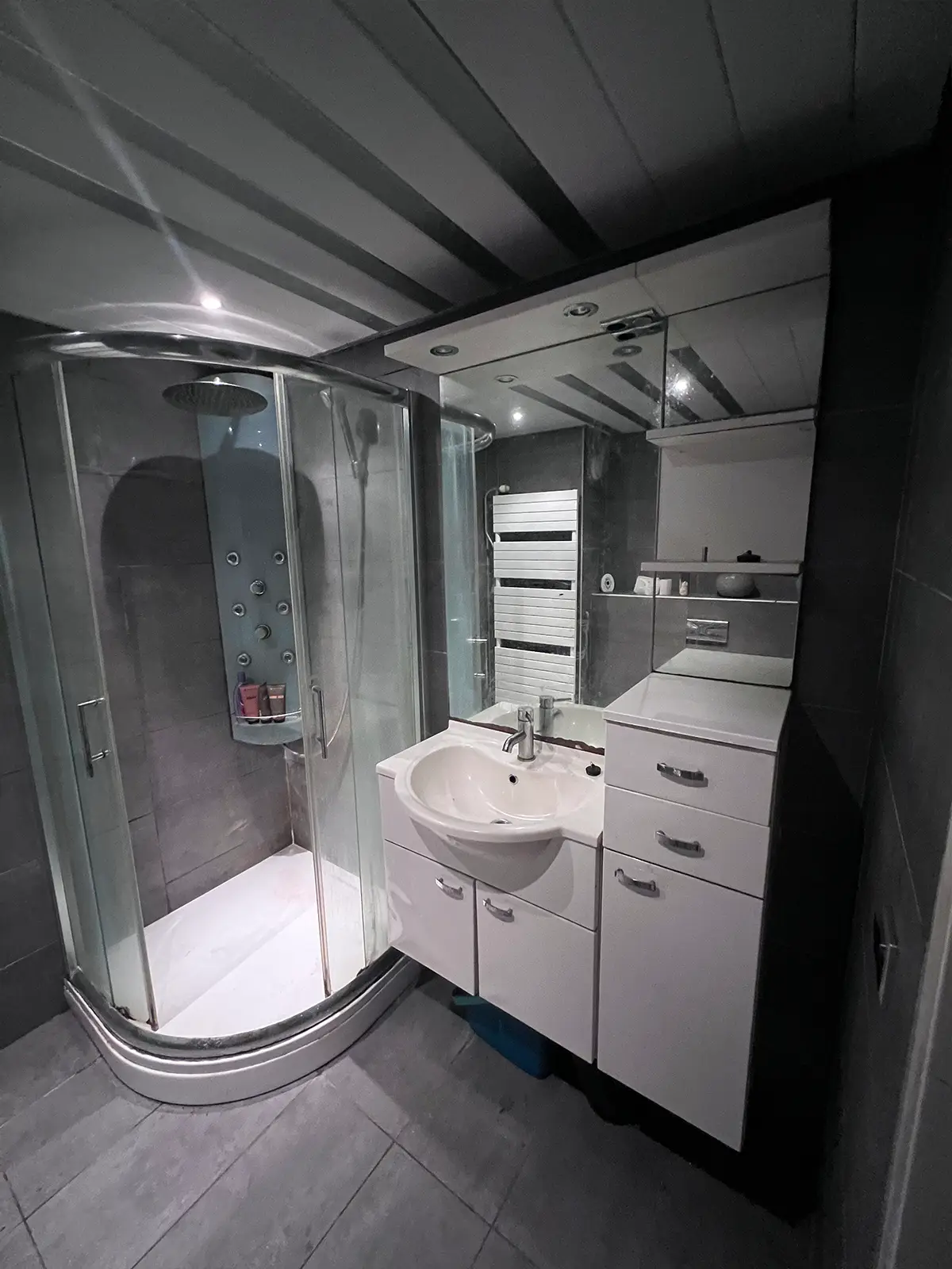 Compacte moderne badkamer met douchecabine, grijze tegels en wit badkamermeubel.