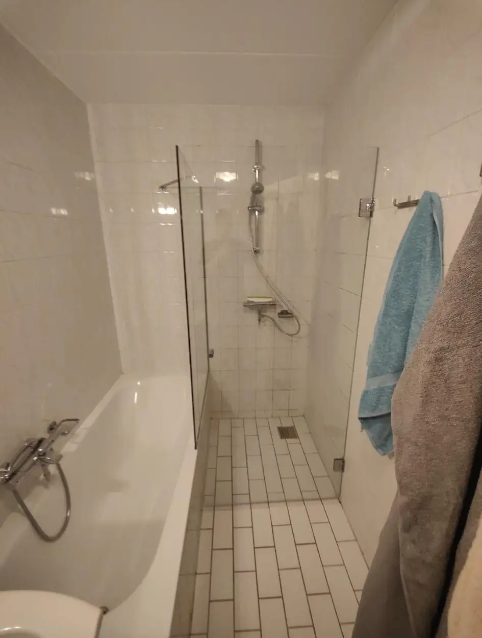 Compacte badkamer met ligbad, glazen douchewand en witte wandtegels.