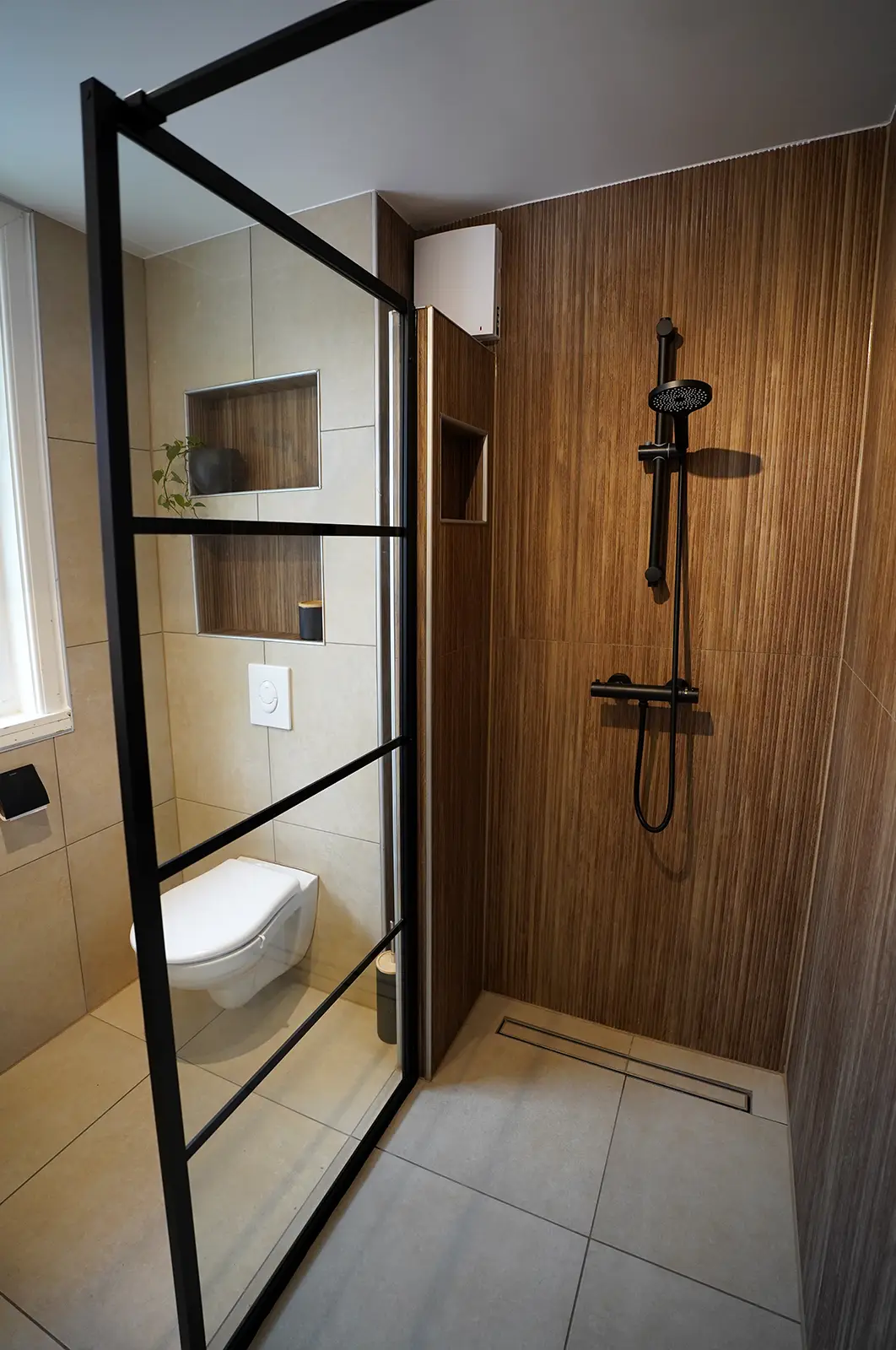 Moderne inloopdouche met houtlook wandpanelen, zwarte douchearmaturen en glazen douchewand met zwart frame.