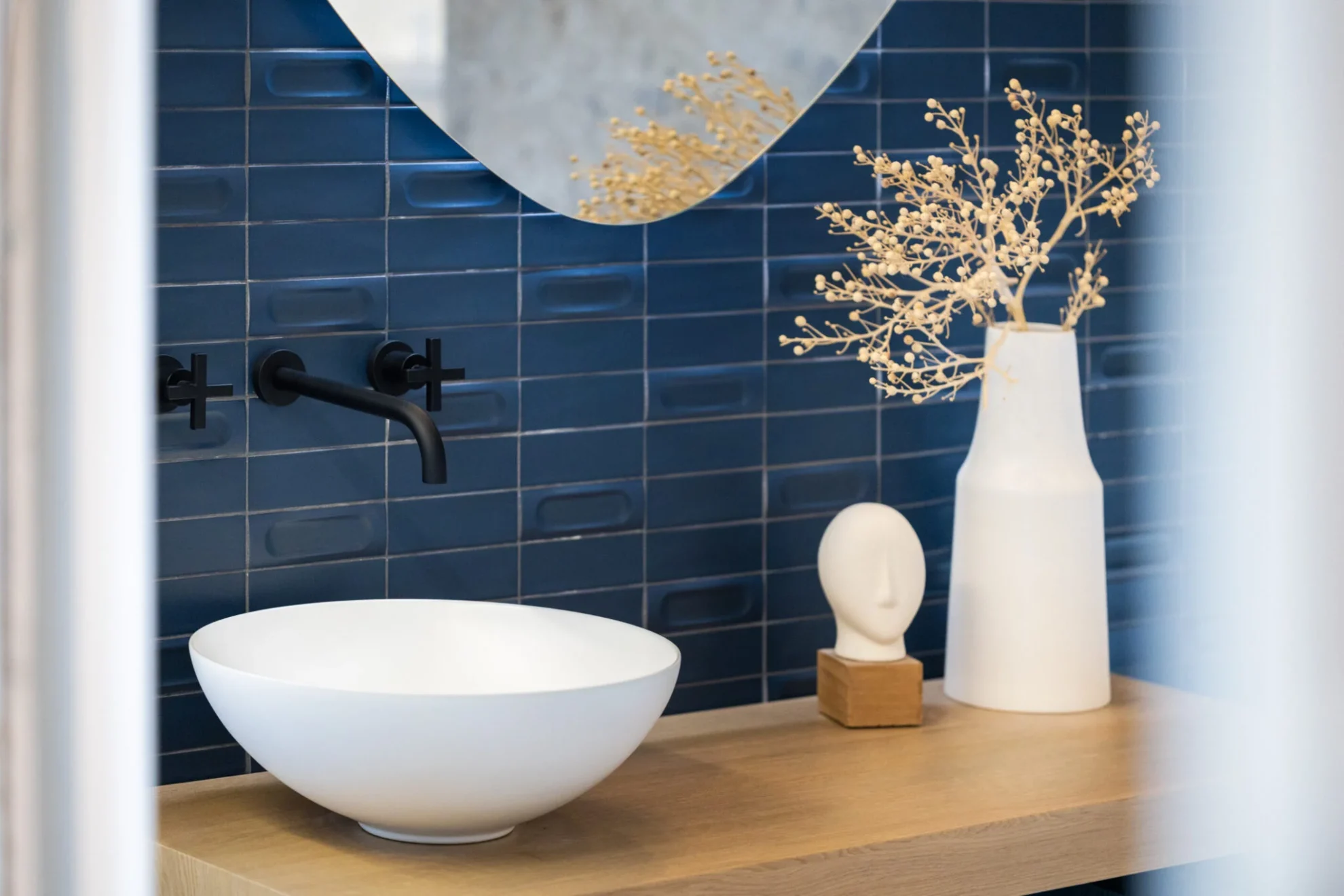Moderne wastafel met matzwarte kraan, blauwe wandtegels en houten badkamermeubel.