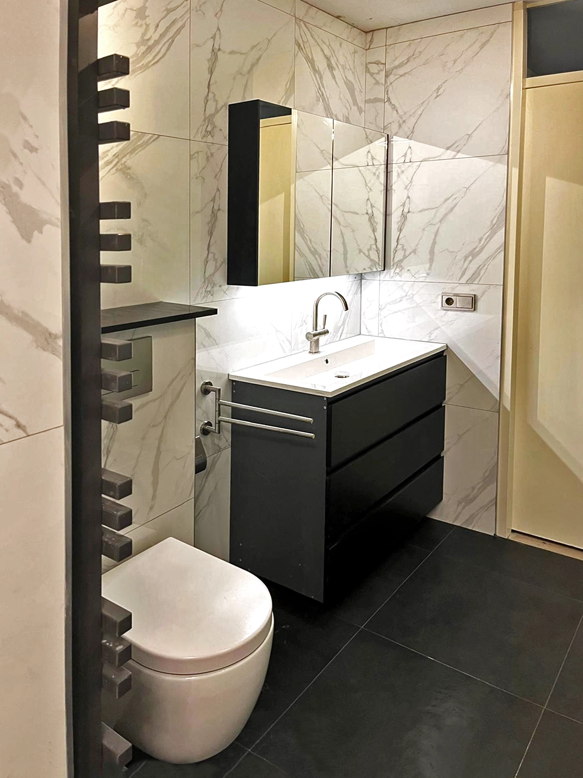 Moderne badkamer met zwart badkamermeubel, marmerlook wandtegels en zwevend toilet.