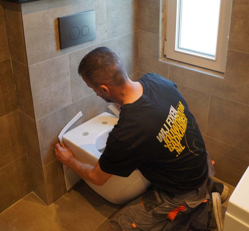 Monteur installeert een hangend toilet in een moderne badkamer met grijze wandtegels.