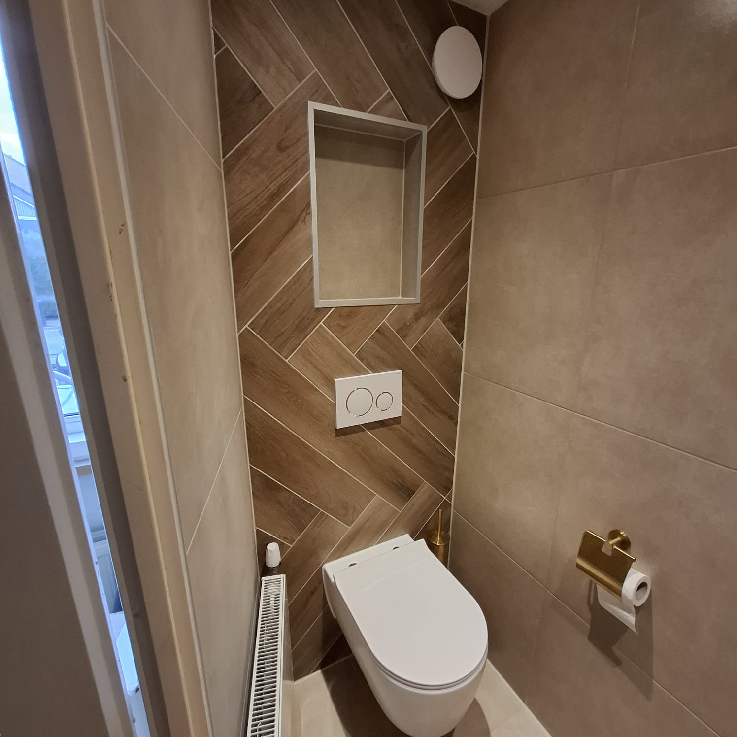 Modern toilet met houtlook visgraattegels, zwevend toilet en ingebouwde nis.