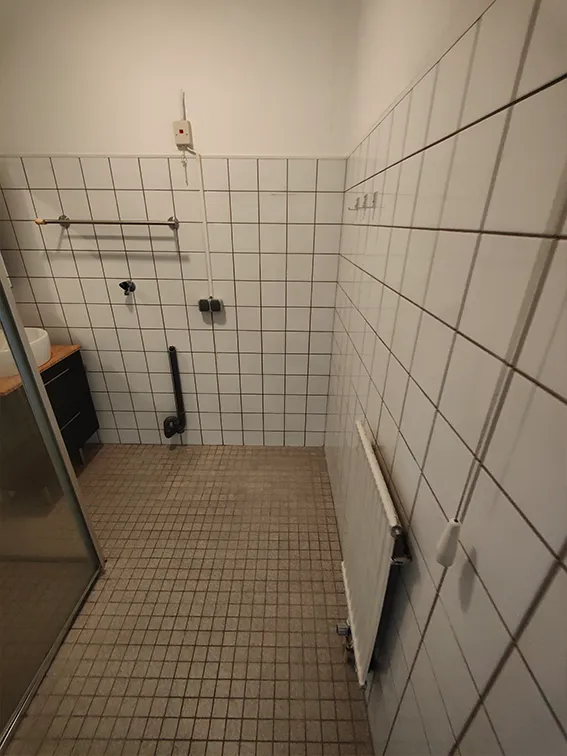 Eenvoudige badkamer met witte wandtegels, mozaïekvloer en douchecabine.