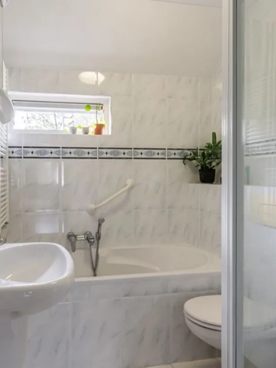 Compacte badkamer met ligbad, witte wandtegels en zwevend toilet.