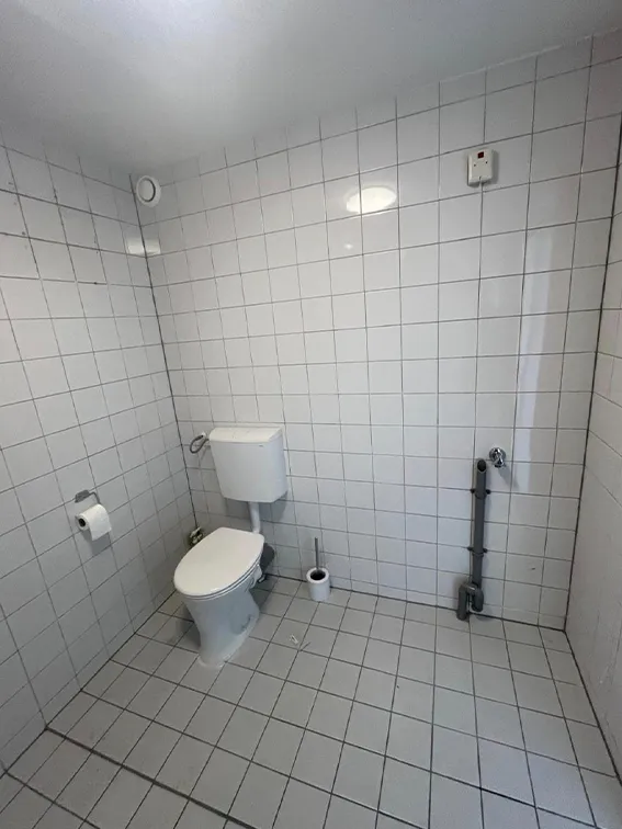Eenvoudige toiletruimte met witte wandtegels, staand toilet en minimalistische afwerking.