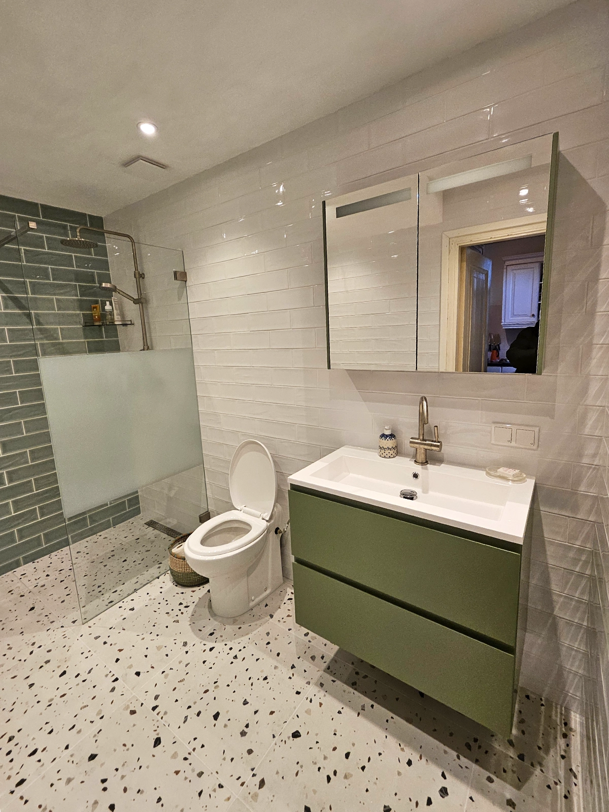 Moderne badkamer met groene wastafelkast, terrazzo vloer en glazen inloopdouche.