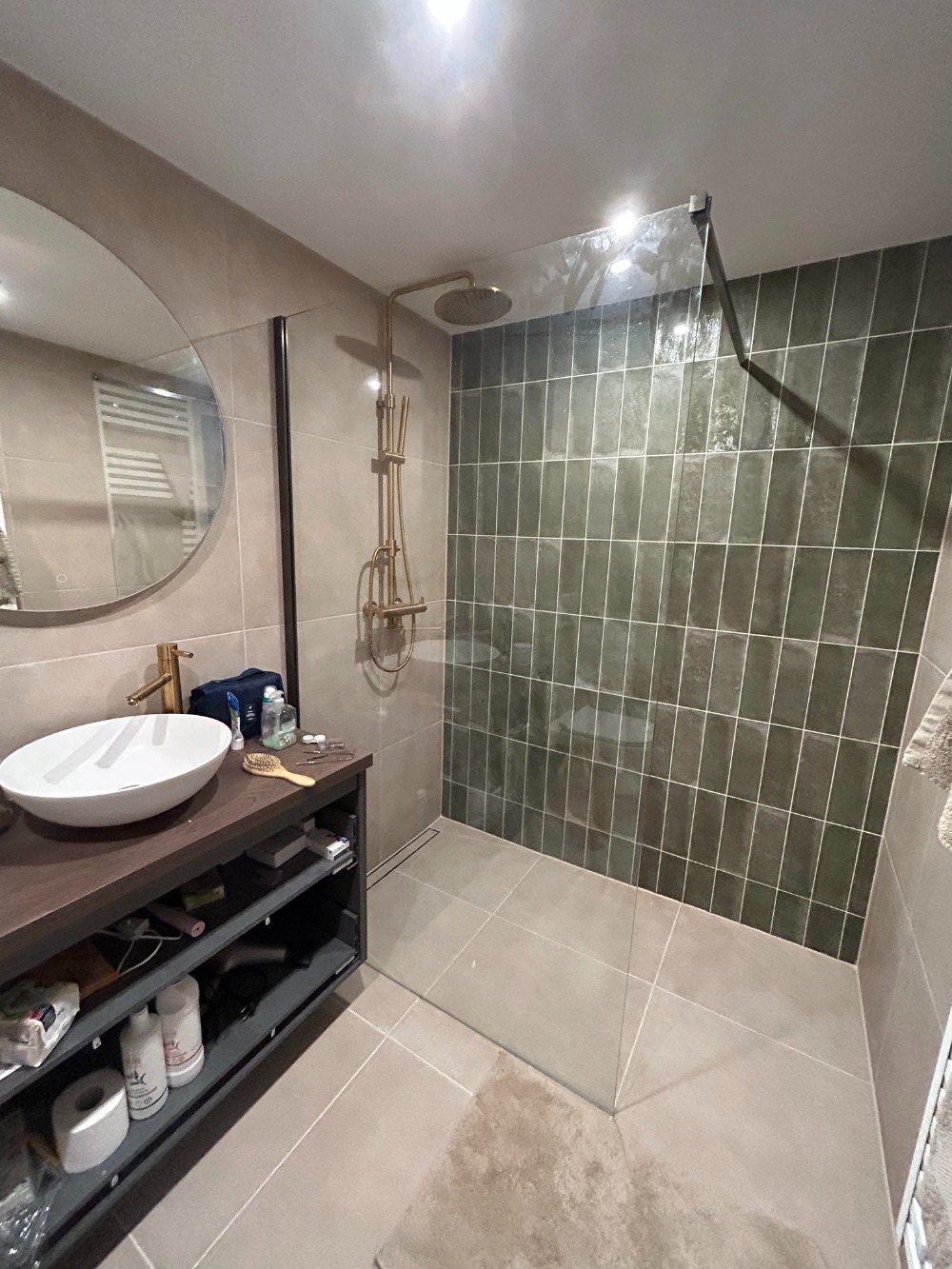 Moderne badkamer met groene wandtegels, glazen inloopdouche en houten badkamermeubel met opbouwwastafel.