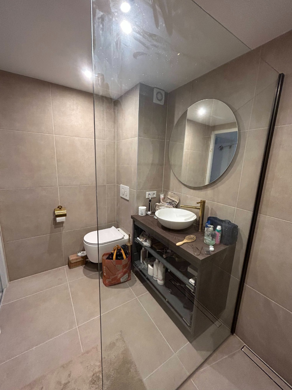 Moderne badkamer met glazen inloopdouche, ronde spiegel en houten badkamermeubel met opbouwwastafel.