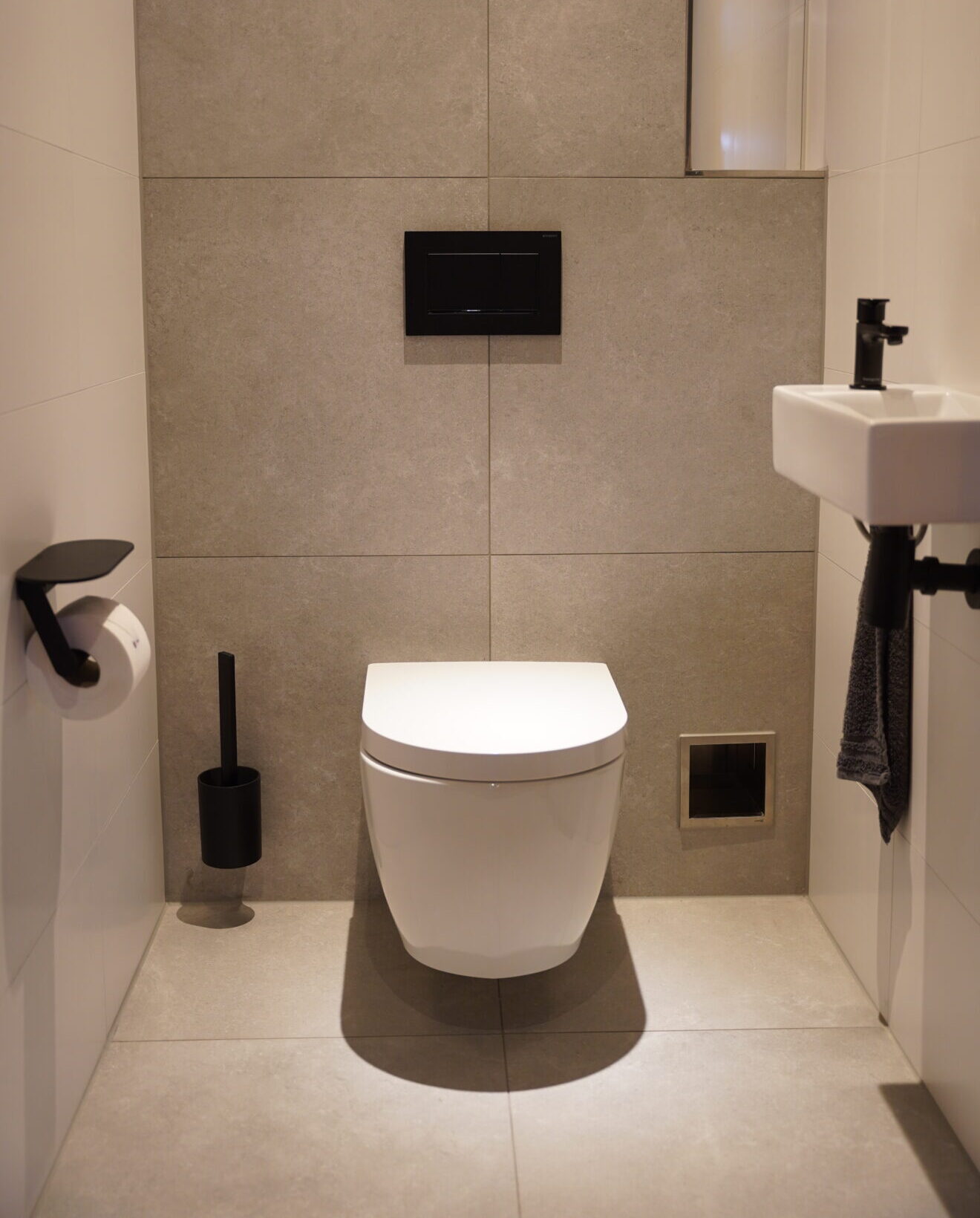 Moderne toiletruimte met zwevend toilet, grijze wandtegels en zwarte accessoires.