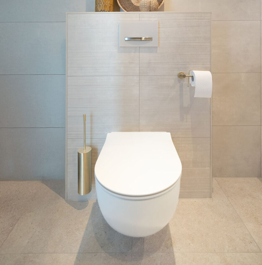 Zwevend toilet met goudkleurige accessoires in een moderne badkamer met lichte wandtegels.