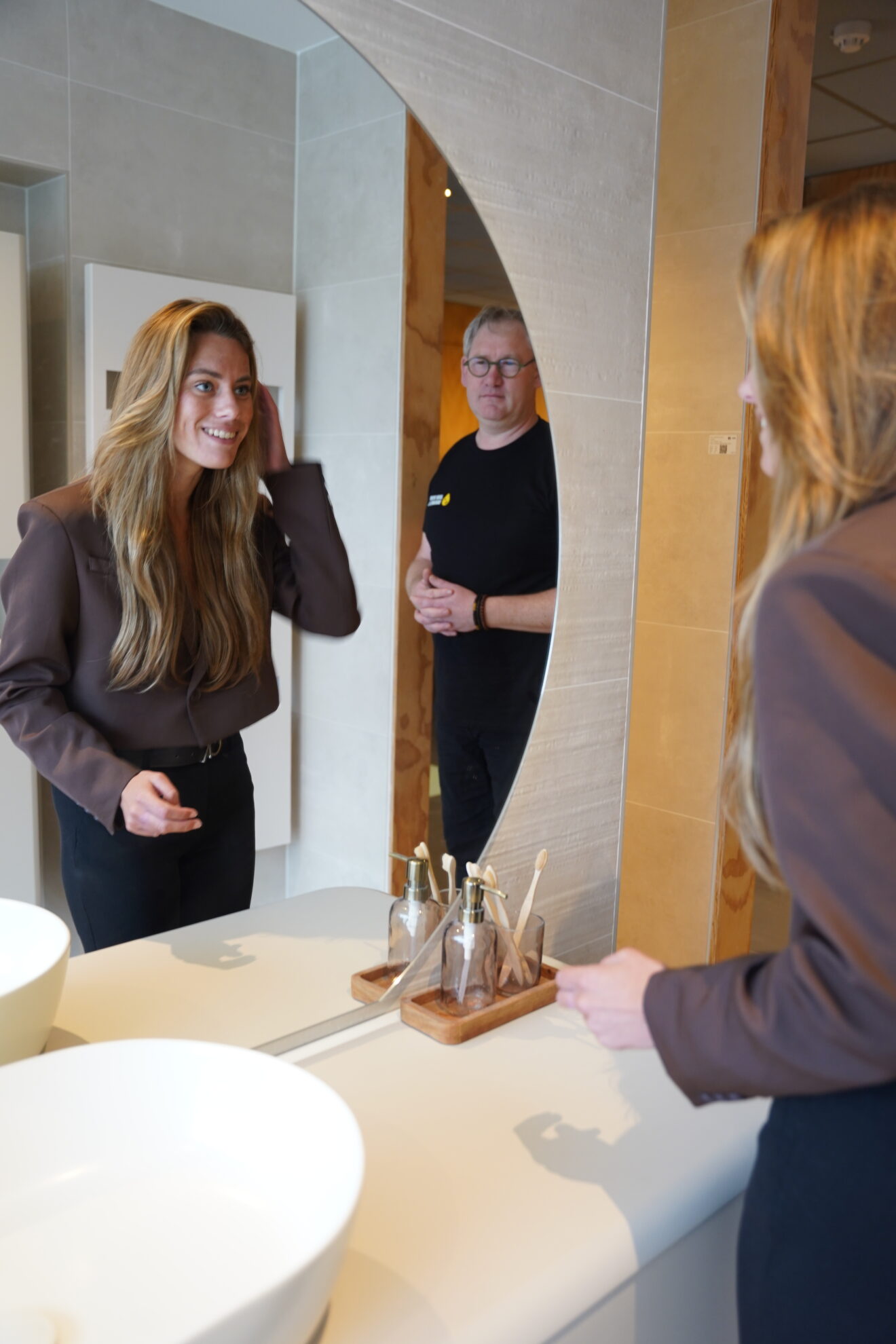 Klant bekijkt zichzelf in een moderne badkamerspiegel tijdens advies in een luxe showroom.