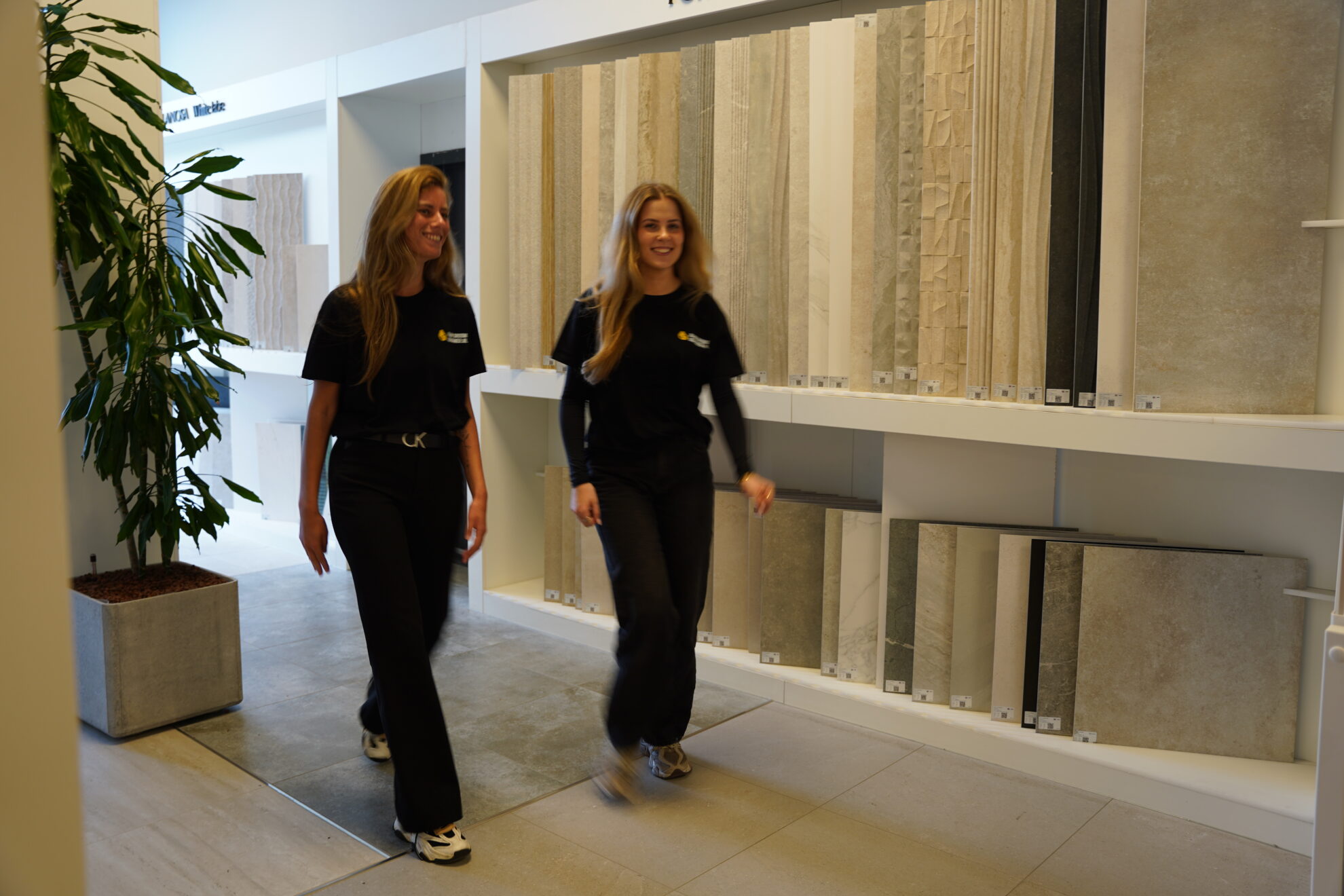 Medewerkers van Jouw Droombadkamer lopen door een moderne tegelshowroom met diverse tegelcollecties.