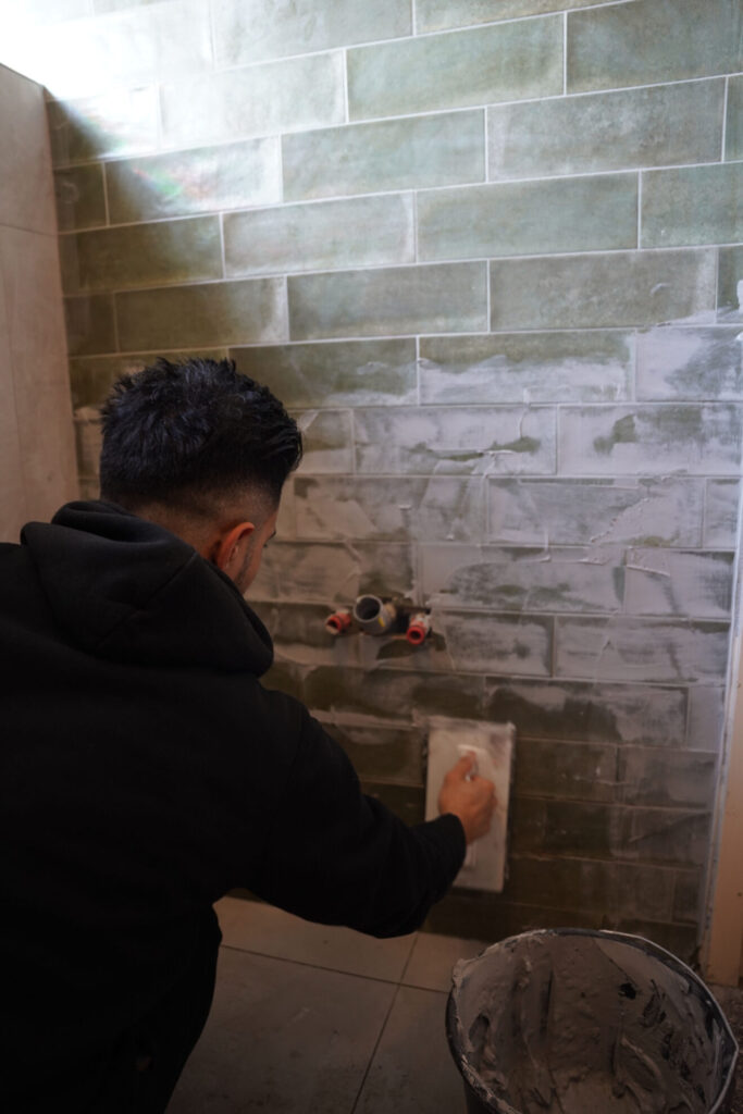 Tegelzetter werkt aan het voegen van groene wandtegels tijdens een badkamerrenovatie.