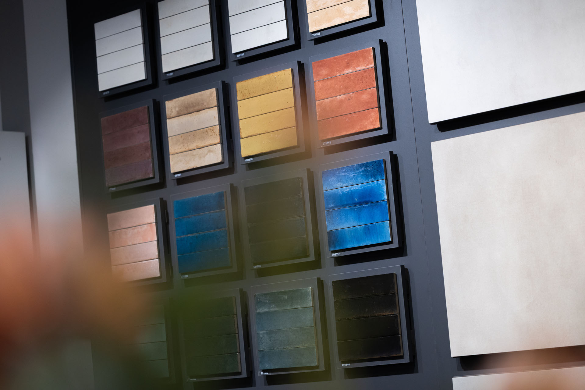 Wand met verschillende tegelstalen in warme, donkere en blauwe tinten in een badkamer showroom.