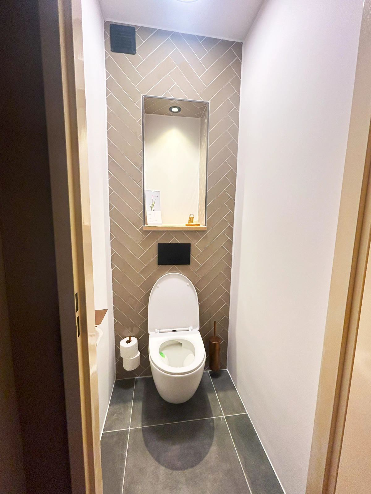 Modern toilet met visgraat wandtegels, ingebouwde nis en donkere vloertegels.