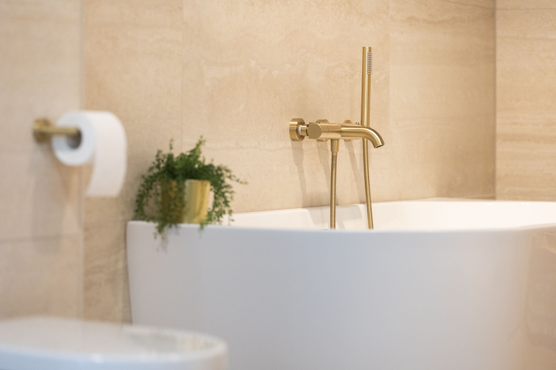 Vrijstaand bad met gouden badkamerkraan in luxe beige badkamer