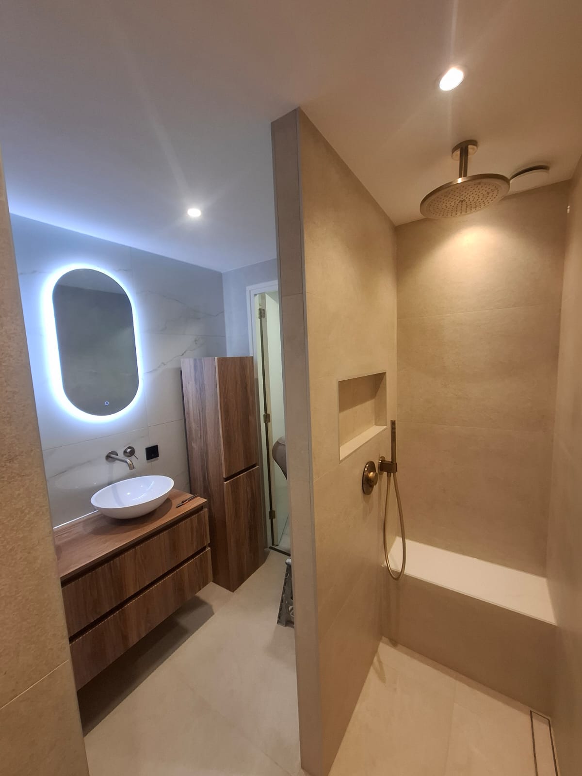 Moderne badkamer met inloopdouche, regendouche, houten wastafelmeubel en verlichte badkamerspiegel.
